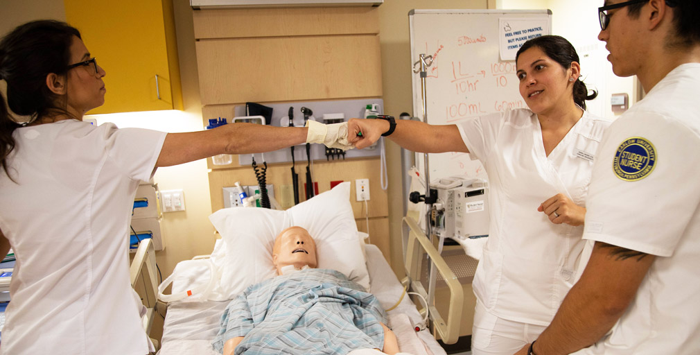 Two nurses in training lab giving fist bump