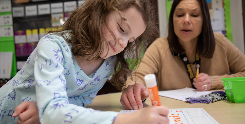Teacher coaching young child to write the alphabet